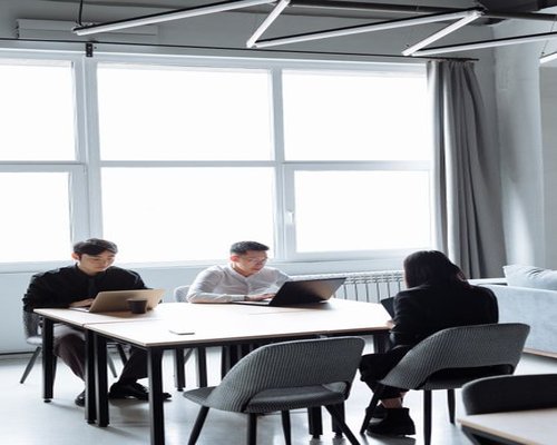 A modern shared community workspace in Mexico City with large glass windows and natural daylight flowing over wooden desks